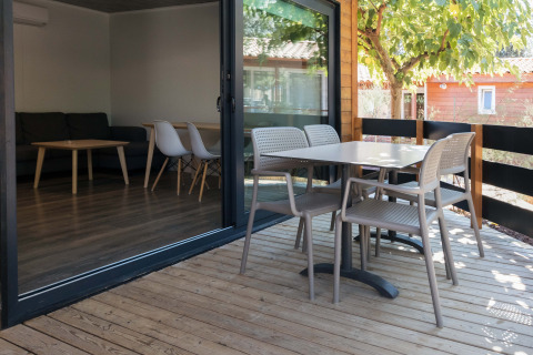 Wooden deck terrace of Bungalow Quermany at Camping Mas Patoxas, Spain, with table and chairs outside.