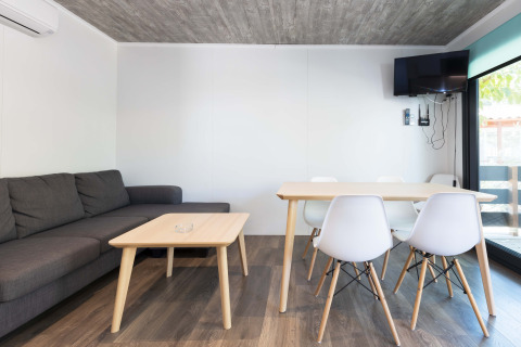 Modern living area in Bungalow Quermany at Camping Mas Patoxas, Spain, with sofa, dining table and wall TV.