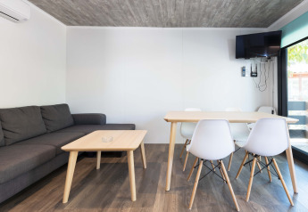 Soggiorno moderno nel Bungalow Quermany al Camping Mas Patoxas, Spagna, con divano, tavolo e TV a muro.