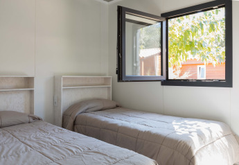 Twee eenpersoonsbedden in een heldere kamer met open raam in Bungalow Quermany, Camping Mas Patoxas, Spanje.