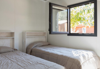 Dos camas individuales en una habitación luminosa con ventana abierta en Bungalow Quermany, Camping Mas Patoxas, España.