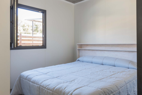 Camera luminosa del Bungalow Quermany al Camping Mas Patoxas, Spagna, con letto matrimoniale e finestra aperta.
