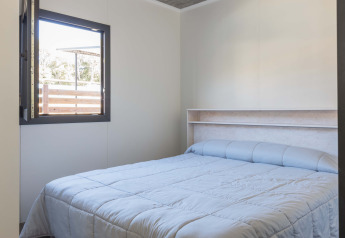 Dormitorio luminoso en Bungalow Quermany de Camping Mas Patoxas, España, con cama doble y ventana abierta.