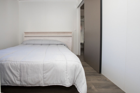 Camera da letto con letto matrimoniale e piumone grigio nel Bungalow Quermany al Camping Mas Patoxas in Spagna.
