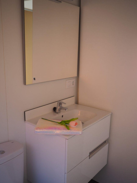 Baño moderno en el Bungalow Quermany, Camping Mas Patoxas, España, con lavabo blanco y espejo amplio.
