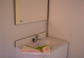 Baño moderno en el Bungalow Quermany, Camping Mas Patoxas, España, con lavabo blanco y espejo amplio.
