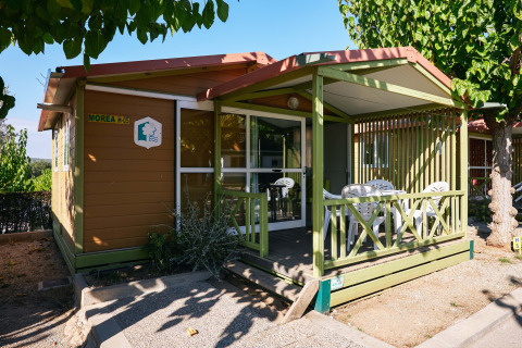 Vista exterior del Bungalow Morea, un acogedor chalet de madera con terraza cubierta y sillas de jardín.