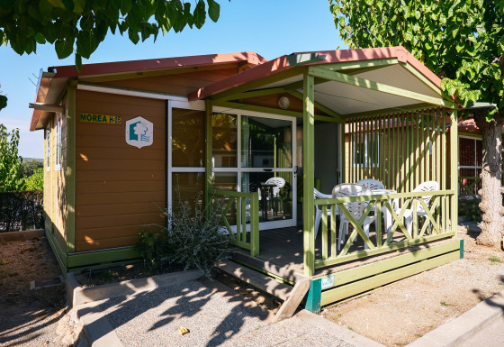 Vista exterior del Bungalow Morea, un acogedor chalet de madera con terraza cubierta y sillas de jardín.