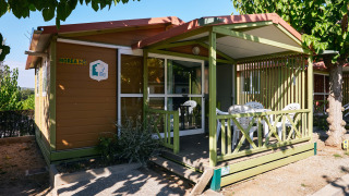Vista exterior del Bungalow Morea, un acogedor chalet de madera con terraza cubierta y sillas de jardín.
