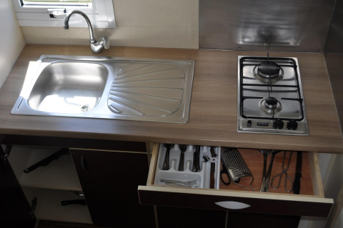 Keukenblad in Bungalow Morea, Camping Mas Patoxas, met spoelbak, gasvuur en open lade met keukengerei.