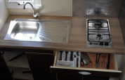 Keukenblad in Bungalow Morea, Camping Mas Patoxas, met spoelbak, gasvuur en open lade met keukengerei.