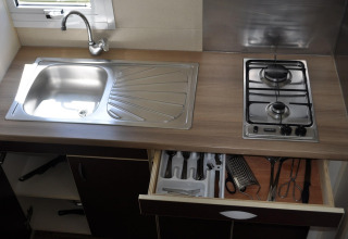Keukenblad in Bungalow Morea, Camping Mas Patoxas, met spoelbak, gasvuur en open lade met keukengerei.