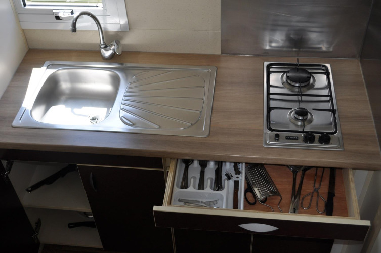 Kitchen countertop in Bungalow Morea, Camping Mas Patoxas, featuring sink, stove, and open utensil drawer.