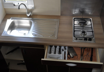 Encimera de cocina en Bungalow Morea, Camping Mas Patoxas, con fregadero, estufa y cajón de utensilios abierto.