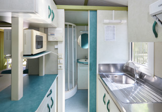 Modern kitchen and bathroom in Bungalow Morea at Camping Mas Patoxas, Spain, with microwave and sink view.