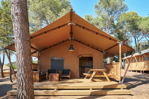 Tenda safari Glamping Tramuntana con terrazza in legno, tavolo da picnic e poltrone tra i pini.