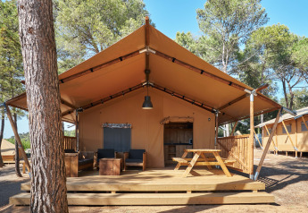 Tenda safari Glamping Tramuntana con terrazza in legno, tavolo da picnic e poltrone tra i pini.