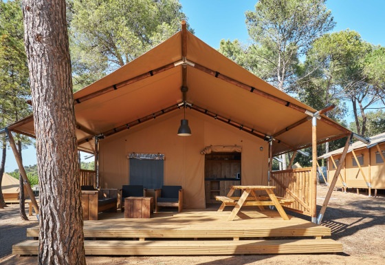 Tienda safari Glamping Tramuntana con terraza de madera, mesa de picnic y sillas bajo pinos.
