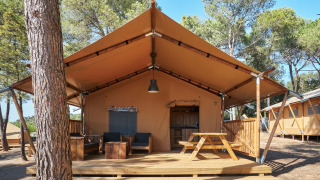 Tienda safari Glamping Tramuntana con terraza de madera, mesa de picnic y sillas bajo pinos.