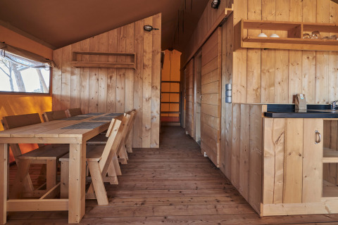 Interni in legno della tenda safari Glamping Tramuntana al Camping Mas Patoxas in Spagna, con tavolo e cucina.