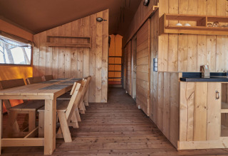 Interni in legno della tenda safari Glamping Tramuntana al Camping Mas Patoxas in Spagna, con tavolo e cucina.