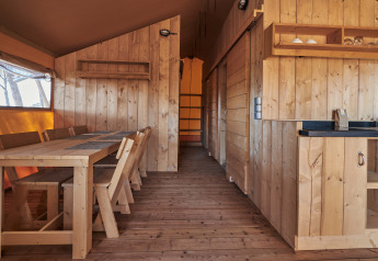Interior de madera de la tienda safari Glamping Tramuntana en Camping Mas Patoxas, España, con comedor y cocina.