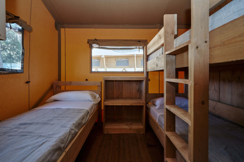 Interior of a safari tent with a single bed and wooden bunk beds at Glamping Tramuntana, Spain.