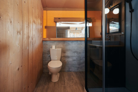 Baño con paredes de madera, inodoro y ducha en la tienda Glamping Tramuntana en Camping Mas Patoxas, España.