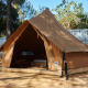 Teltet Glamping Nature Tent i teepee-stil, sat op på en træplatform omgivet af natur og træer.