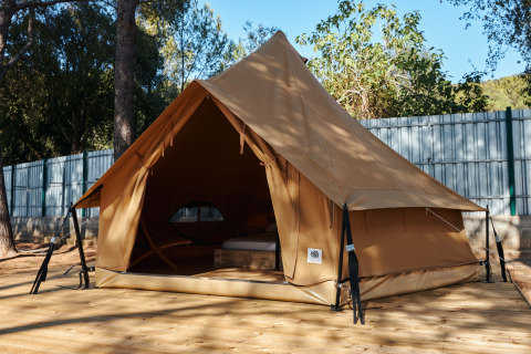 Tente Glamping Nature Tent de style tipi, installée sur une plateforme en bois entourée de nature et d’arbres.