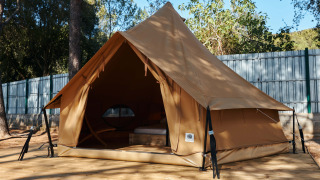 Glamping Nature Tent in stile teepee, montata su piattaforma di legno e circondata dalla natura e alberi.