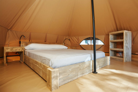 Interno della Glamping Nature Tent al Camping Mas Patoxas in Spagna, con letto e mobili rustici in legno.