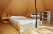 Interno della Glamping Nature Tent al Camping Mas Patoxas in Spagna, con letto e mobili rustici in legno.