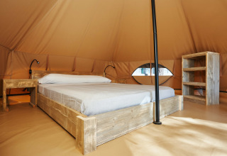 Interno della Glamping Nature Tent al Camping Mas Patoxas in Spagna, con letto e mobili rustici in legno.