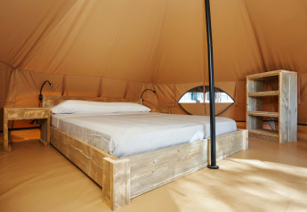 Interno della Glamping Nature Tent al Camping Mas Patoxas in Spagna, con letto e mobili rustici in legno.