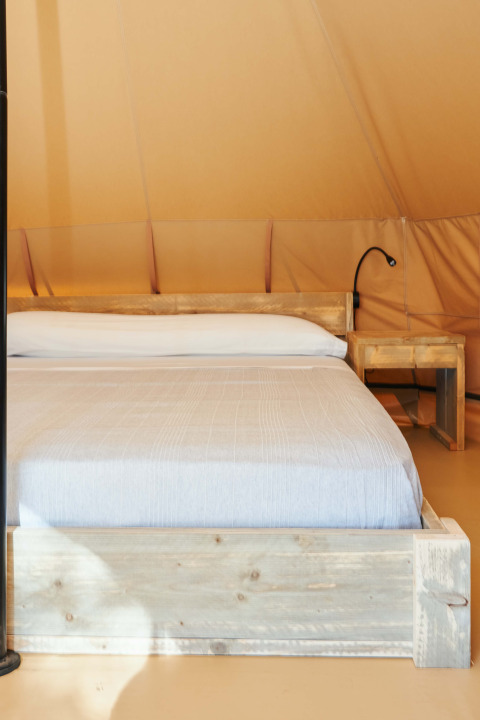 Interior de la tienda Glamping Nature en Camping Mas Patoxas, España, con cama de madera y mesilla.