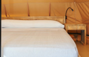 Interior de la tienda Glamping Nature en Camping Mas Patoxas, España, con cama de madera y mesilla.