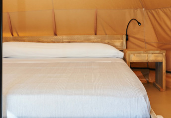 Interior de la tienda Glamping Nature en Camping Mas Patoxas, España, con cama de madera y mesilla.