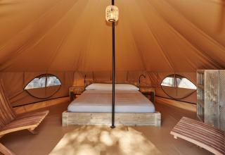 Vista interior de la tienda Glamping Nature en Camping Mas Patoxas, España, con cama y sillas de madera.