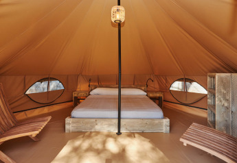 Vista interior de la tienda Glamping Nature en Camping Mas Patoxas, España, con cama y sillas de madera.