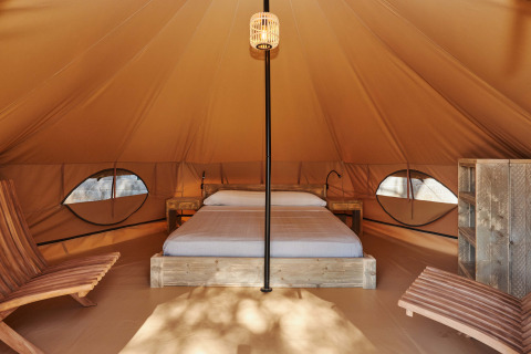 Vista interna della Glamping Nature Tent a Camping Mas Patoxas in Spagna con letto e sedie in legno.