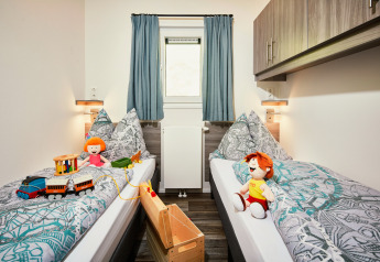 Kinderkamer in Panorama Chalets met twee enkele bedden, poppen, speelgoed en warme aankleding.