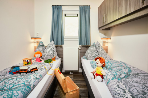 Camera per bambini a Panorama Chalets con due letti singoli, giocattoli, bambole e arredo accogliente.