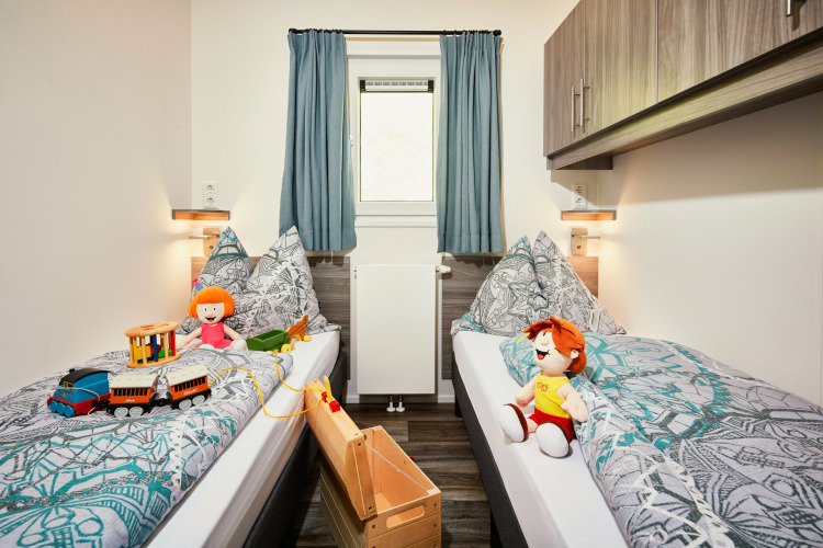 Habitación infantil en Panorama Chalets con dos camas individuales, juguetes, muñecos y decoración acogedora.