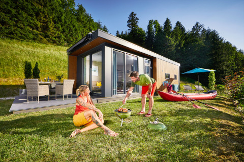 Deux personnes profitent d’un barbecue devant un Panorama Chalet moderne entouré de verdure et de forêt.
