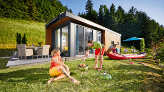 Twee mensen genieten van een barbecue bij een modern Panorama Chalet, omgeven door groene natuur.