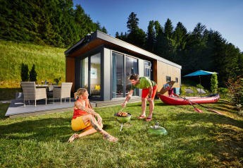 To personer hygger sig ved grill foran et moderne Panorama Chalet omgivet af natur og grønne bakker.