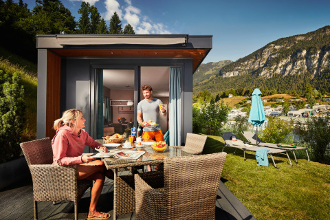 Dos personas desayunan al aire libre en un Panorama Chalet rodeado de montañas y ambiente acogedor.