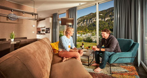 A couple relax comfortably in a modern living room with mountain views at Panorama Chalets.