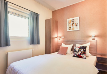 Lichte slaapkamer in Panorama Chalets met tweepersoonsbed, moderne inrichting en raam met gordijnen.